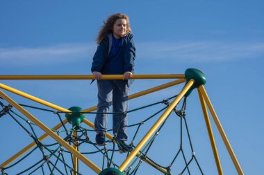 Çocuk dışarı tırmanıyor. Oyun parkına tırmanan aktif bir çocuk. Çocuk parka tırmanıyor. Mutlu çocuk dışarıda oynamaktan hoşlanıyor. Sevimli çocuk oyun alanında eğleniyor. Çocuk parka tırmanıyor