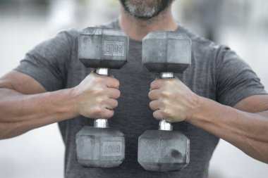 Dambıllar kol kola. Yetişkin bir adamın dambılları dışarı kaldırması. Kol kasları dambıl egzersizi yapıyor. Kol halteri tutun. Dambılı bir erkek kolunun yakın çekimi.