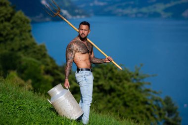 Çiftlikte çalışan taşralı seksi adam. Güneşin altındaki bir tarlada çalışan çiftçi. Çimenli bir tarlada yaba ile çiftçi. Yeşil bir alanda kırsal bir işçi. Çiftlik ortamında süt tenekesi olan çalışkan bir adam.