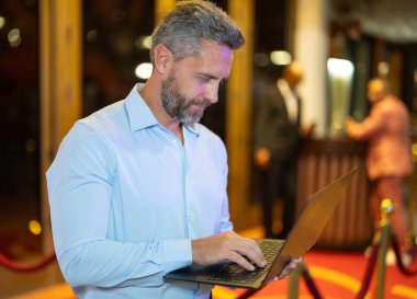 Gece sokakta dizüstü bilgisayar kullanan bir iş adamı. İş adamı dışarıda dizüstü bilgisayarda çalışmayı planlıyor. İşadamı, neon şehir ışıkları altında dizüstü bilgisayarda geziniyor. Serbest çalışan bir iş adamı. Gece işi.