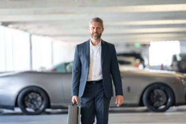 Zengin bir iş adamı. Zengin işadamı başarısının tadını çıkarıyor. Şık takım elbiseli lüks iş adamı. Pahalı arabanın önündeki zengin adam. Lüks iş seyahati. Klasik takım elbiseli, kendinden emin zengin bir iş adamı.