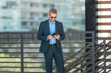 Finans uzmanı bir kontratı inceliyor. Tabletli bir iş adamı. Dışarıda tablet kullanan bir iş adamı. Olgun iş adamı finans verilerini kontrol ediyor. Tabletteki zengin işadamı gözden geçirme sözleşmesi