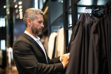 Bir adam butikte alışveriş yaparken klasik bir terzi kıyafeti giyer. Başarılı bir iş adamı için klasik bir kıyafet. Takım elbiseli modaya uygun bir mağaza. Takım elbise seçen bir iş adamı. Bir erkek resmi etkinlik için takım elbise seçer.