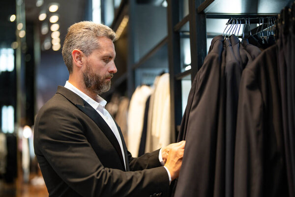Мужчина носит классический костюм, когда делает покупки в бутике. Классический костюм для успешного бизнесмена. Модный магазин с костюмами. Бизнесмен выбирает костюм. Мужчина выбирает костюм для официального мероприятия