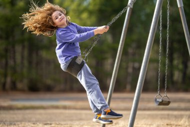 Dışarıda sallanan mutlu çocuk. Salıncakta gülen çocuk. Oyun bahçesinde oynayan neşeli çocuk. Heyecanlı çocuk salıncakta sallanıyor. Yaz parkındaki sevimli çocuk. Parkta sallanan oyuncu çocuk. Mutlu çocukluk