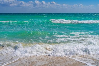 Turkuaz deniz dalgası hareketi. Yaz plajı. Sakin deniz. Lüks sahil beldesi. Parlak gökyüzü ve sahilde dalgalar. Güzel köpüklü kıyı şeridi. Deniz arka planı. Mavi okyanus. Kumlu okyanus plajı. Deniz dalgaları