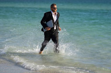 Yaz seyahati. İş başarısı. Serbest çalışma, uzaklık, online çalışma, e-çalışma. Takım elbiseli bir işadamı deniz suyunda dizüstü bilgisayarla çalışıyor. Komik bir yaz işi. Serbest seyahat.