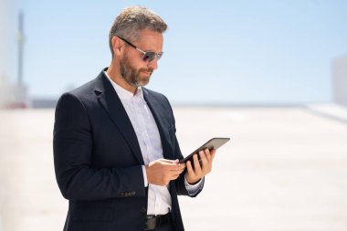 Dışarıda tablet kullanan bir iş adamı. Tabletle başarılı bir iş adamı. Şirket lideri iş adamı tablet üzerinde çalışıyor. Zarif iş adamı tableti kontrol ediyor. Olgun iş adamı belgeleri inceliyor