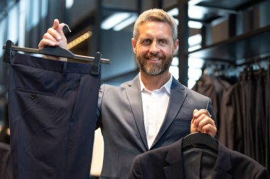 Takım elbiseli, takım elbiseli bir adam. Bir iş adamı mağazada şık bir takım elbise seçer. Modayı takip eden bir müşteri resmi kıyafet alırken ceketi inceler. Klasik kıyafetli çekici bir manken.