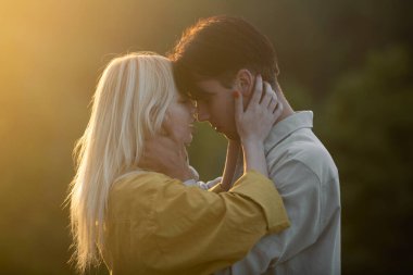 Şehvetli aşıklar gün batımında sarılıp öpüşüyorlar. Genç şehvetli kız arkadaşı, erkek arkadaşından tutkulu bir öpücük aldığı için mutlu. Yakışıklı genç adam kadınını kucaklıyor ve öpüyor.