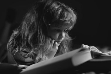 Yatakta uzanmış kitap okuyan sevimli bir çocuk. Çocuğun gelişimi. Akıllı çocuk.