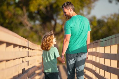 Baba ve Oğul 'un ağaçlık köprüde yürüdüğü arka manzara. Baba oğul konuşuyor, doğada eğleniyorlar. Ebeveynlik, ebeveynlik, çocukluk ve aile hayatı kavramı
