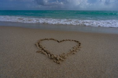Kalp kumda çizilmiş. Dalgalar kalp şeklinde bir işaret oluşturuyor. Kumsalda aşk. Romantik yaz. Kumdan yapılmış bir kalp. Aşk ve okyanus dalgaları