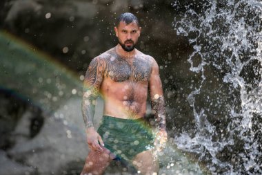 Doğada güçlü bir adam. Şelalenin altına sıçrayan seksi üstsüz adam. Formda ve güçlü bir erkek vücudu. Seksi manken yazın tadını çıkarıyor. Erkek güzeli. Su damlalı kaslı gövde. Manzarada üstsüz bir adam