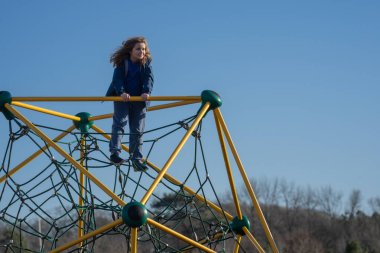 Tırmanışta oynayan çocuk. Oyun parkına tırmanan aktif bir çocuk. Çocuk parka tırmanıyor. Mutlu çocuk dışarıda oynamaktan hoşlanıyor. Sevimli çocuk oyun alanında eğleniyor. Çocuk parka tırmanıyor
