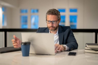 Ofisinde dizüstü bilgisayarı olan bir iş adamı. Modern ofiste çalışan uzaktan kumandalı personel. İş adamı çevrimiçi toplantıda. İnternette çalışan İspanyol iş adamı. İş yerinde laptop kullanan olgun bir iş adamı