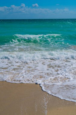 Turkuaz deniz dalgası hareketi. Yaz plajı. Sakin deniz. Deniz kıyısındaki tatil. Parlak gökyüzü ve sahilde dalgalar. Güzel köpüklü kıyı şeridi. Deniz arka planı. Mavi okyanus. Kumlu okyanus plajı. Deniz dalgaları
