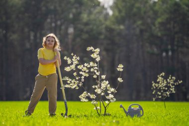 Çocuk bahçeye bir ağaç dikti. Çocuk kürek ve bitki ağacıyla toprak kazıyor. Çocuk bahçıvan meyve ağaçlarıyla ilgileniyor. Çocuklarla ağaç dikmek. Yeşil için çocuk bitkisi. Çocuklar için bahçe işleri. Çocukluk gelişimi