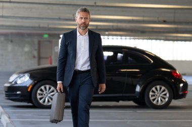 Lüks bir arabanın yanında zengin bir iş adamı. Takım elbiseli zengin bir iş adamı. Şehirdeki başarılı zengin iş adamı. Kendine güvenen bir iş adamı. Başarı işi ve zenginlik. İş adamı sokakta yürüyor