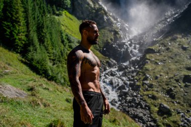 Yaz tatilindeki erkek turist. Yaz tatilinde çıplak gövdeli yakışıklı bir adam. Dışarıda seksi bir yürüyüşçü var. Şelale manzarasında yürüyen bir turist. İnsan Seyahati ve doğa