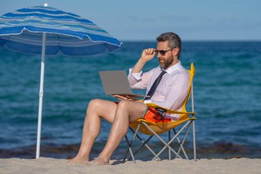 İş tatili. Yaz tatilinde yakışıklı bir iş adamı. İş adamı elinde dizüstü bilgisayarla deniz sahilinde dinleniyor. Yaz işi. Yaz Denizi Sahili 'nde serbest yazar. Yaz haftasonu ve uzak bağımsız çalışma