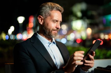 Çevrimiçi gece işi. Dışarıda tablet üzerinde çalışan bir iş adamı. Tabletli bir iş adamı. Gece sokağında tabletli bir iş adamı. Tablet kullanan bir işadamı, bankta oturur. Gece işi.