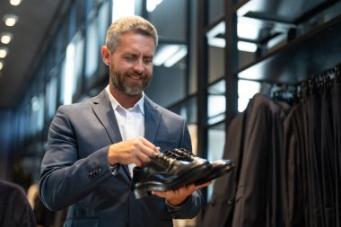 Takım elbiseli şık bir adam bir butikte lüks ayakkabılara hayran. Bir iş adamı bir ayakkabı mağazasında şık ayakkabılar seçer. Resmi görünmek için klasik deri ayakkabılar. Resmi ayakkabılar