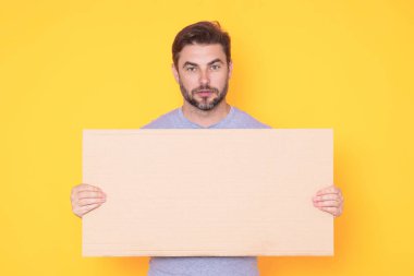 Stüdyonun arka planında boş tahtası olan yakışıklı bir adam. Telif uzayı ile boş tabela gösteren bir adam. Fikir teklifi. Reklamınız. Metin için boş alanı olan boş reklam panosu, modelle