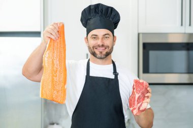 Modern mutfakta, tek başına sağlıklı yiyecekler hazırlayan, balık ve et pişiren, somon ve sığır eti pişiren bir adam. Yakışıklı adam evde taze balık, et, somon ve sığır eti hazırlıyor.