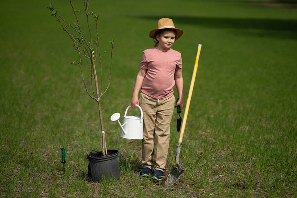 Парень с лопатой в саду. Ребенок выращивает дерево в саду. Ребенок сажает дерево. Маленький садовник с лейкой. Весна сад с детьми