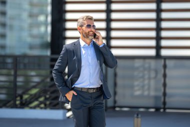 İş adamı yürüyor ve telefonla arıyor. Kendine güvenen bir iş adamının önemli bir çağrısı var. İş görüşmesi. Telefon görüşmesi. Patron telefonla konuşmakla meşgul. Zengin iş adamı. İş çağrısı