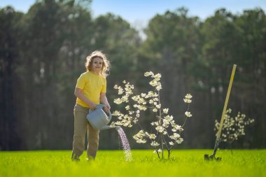 Çocuk bahçeye bir ağaç dikti. Çocuk kürek ve bitki ağacıyla toprak kazıyor. Çocuk bahçıvan meyve ağaçlarıyla ilgileniyor. Çocuklarla ağaç dikmek. Çocuklar için bahçe işleri. Kürek ağacı olan çocuk