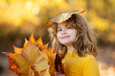 Sonbahar parkında yaprakları olan bir çocuk. Çocuk dışarıda eğleniyor. Sonbaharın tadını çıkarıyorum. Arka planda kal. Sonbahar sonbahar ormanlarında güzel bir sonbahar çocuğunun portresi. Güzel çocuk düşen yapraklarla oynuyor.