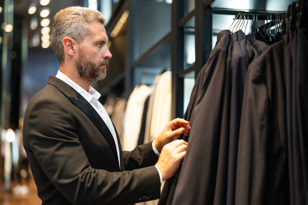 Мужчина носит классический костюм, когда делает покупки в бутике. Классический костюм для успешного бизнесмена. Модный магазин с костюмами. Бизнесмен выбирает костюм. Мужчина выбирает костюм для официального мероприятия