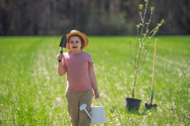 Bahar bahçesi. Çocuk kürekle toprak kazıyor. Bahçesinde ağaç bitkileri olan bir çocuk. Bahar bahçesinde çalışan çocuklar. Bahçe aletleri. Çocuk bahçıvanlığı. Bahçe işliyorum. Çocuk dikme ağacı. Çiftlikteki çocuk