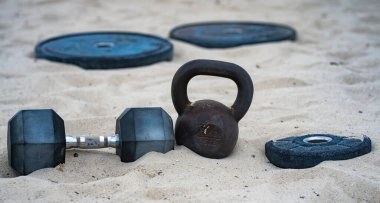 Kettlebell ve ağırlık arka planı. Ağır ağırlıklarla vücut geliştirme. Dambıllarla park egzersizi. Ağırlıklarla spor sahnesi. Kettlebell, halterler ve halterler. Ağırlık çalışması.