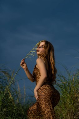 Uzun elbiseli seksi bir kızın moda portresi. Moda elbisesi içinde doğaya poz veren güzel bir genç kadının portresi. Çekici popo modeli kız. Leopar elbiseli romantik bir kadın.