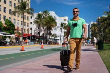 Miami 'nin güneşli sokaklarında bir turist yürüyor. Bir erkek turist, tropikal bir şehirde yaz tatilinin tadını çıkarır. Bavullu bir turist şehir manzarasını keşfediyor. Erkek turist şehirde yürüyor