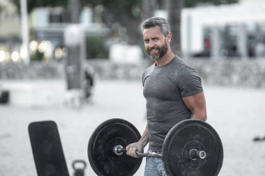 Halteri kaldıran formda bir adam. Halk parkında halterle ağırlık çalışması. Güçlü kollar ve omuzlar halteri kaldırıyor. Spor model halter yapıyor. Açık hava halterleri egzersizleri ile atletik yaşam tarzı