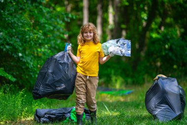 Çöp poşeti dolusu çöp ve çöp maşası olan bir çocuk. Geri dönüşüm kutusuyla ormanda veya parkta plastik atık toplayan sevimli bir çocuk. Çevre aktivistleri. Çevresel koruma ve ekoloji