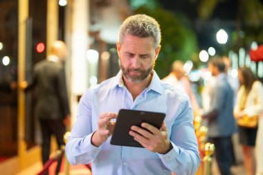 Gece sokakta tablet kullanan bir iş adamı. İş adamı dışarıda tablet üzerinde çalışmayı planlıyor. İşadamı neon şehir ışıkları altında bir tablet üzerinde geziniyor. Serbest çalışan bir iş adamı. Gece işi.