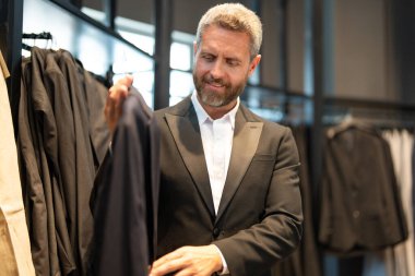 Bir butik danışmanı müşterinin mükemmel takımı bulmasına yardım eder. Lüks bir giysi koleksiyonu. Zarif takım iş adamı için mükemmel. İyi dikilmiş bir takım.