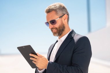 Açık havada tablet kullanan mutlu bir iş adamı. Tabletle başarılı bir iş adamı. Dışarıda tablet üzerinde çalışan bir iş adamı. Zarif iş adamı tableti kontrol ediyor. Dijital aygıt kullanan işadamı