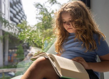 Kütüphanede kitap okuyan sevimli sarışın çocuk. Çocuk ders çalışıyor ve okuyor. Akıllı çocuk kitap okur. Kitaptan küçük bir öğrenci öğreniyor. Çocuk kütüphanede kitap okuyor. Okuma yoluyla bilgi