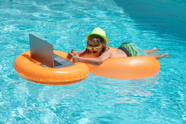 Yaz işi. Çocuk havuzda yüzme ringinde oturuyor ve dizüstü bilgisayar kullanıyor. İnternetten alışveriş, serbest konsept, yaz seyahati.