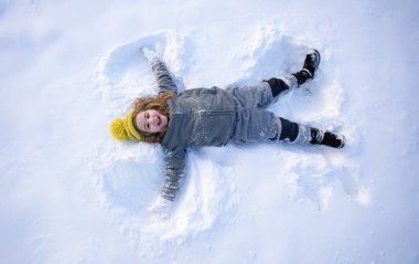 Kış eğlencesi Çocuk kış günü kar meleği yapıyor. Karda yatan mutlu çocuk. Kardaki melek çocuk. Karlı melek kanatlı kış çocukları. Kış gününde gülümseyen bir çocuk. Kar gölü meleğindeki çocuk