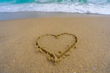 Kalp kumda çizilmiş. Dalgalar kalp şeklinde bir işaret oluşturuyor. Kumsalda aşk. Romantik yaz. Kumdan yapılmış bir kalp. Aşk ve okyanus dalgaları
