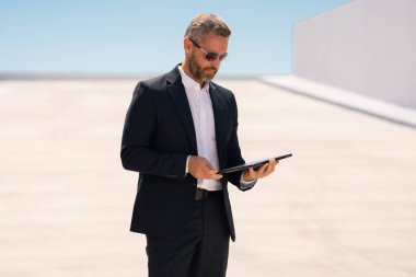 İş adamı dışarıda dizüstü bilgisayar kullanıyor. Dizüstü bilgisayarda çalışan başarılı bir adam. Dizüstü bilgisayarı olan kendinden emin bir iş adamı. İnternette iş. Şehir işadamı dışarıda dizüstü bilgisayardan verileri kontrol ediyor. Takım elbiseli adam internette çalışıyor.