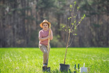 Kürekle ağaç yetiştiren mutlu çocuk. Arka bahçede ağaç yetiştiren bir çocuk. Bahar tarlasında ağaç yetiştiren çocuk. Su kovası ve küreği olan bahçıvan. Bahçe çiftliğinde ağaç yetiştiren çocuk. Çocuklar çalışır.