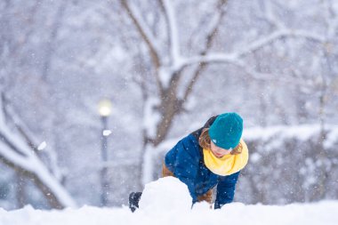 Mutlu Çocuk kışın kardan adam için kartopu yapıyor. Çocuk karda oynuyor. Açık havada aktif kış oyunları. Çocuk karla oynarken eğleniyor. Çocuklar için açık havada kış tatili. Güneşli kış gününde çocuk oyunu